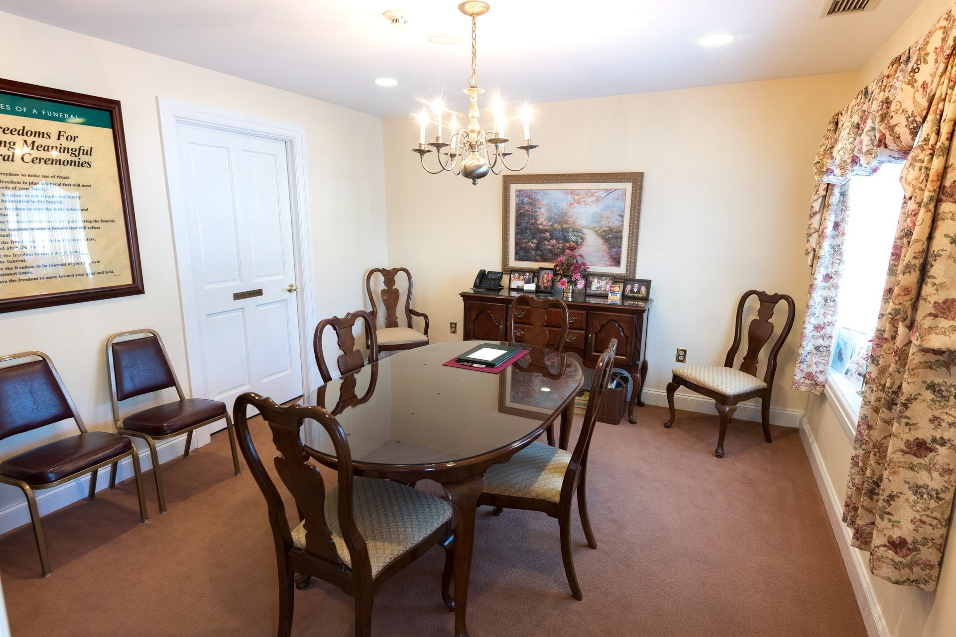Elegant meeting room with chairs around a table, chandelier, framed art, and floral curtains