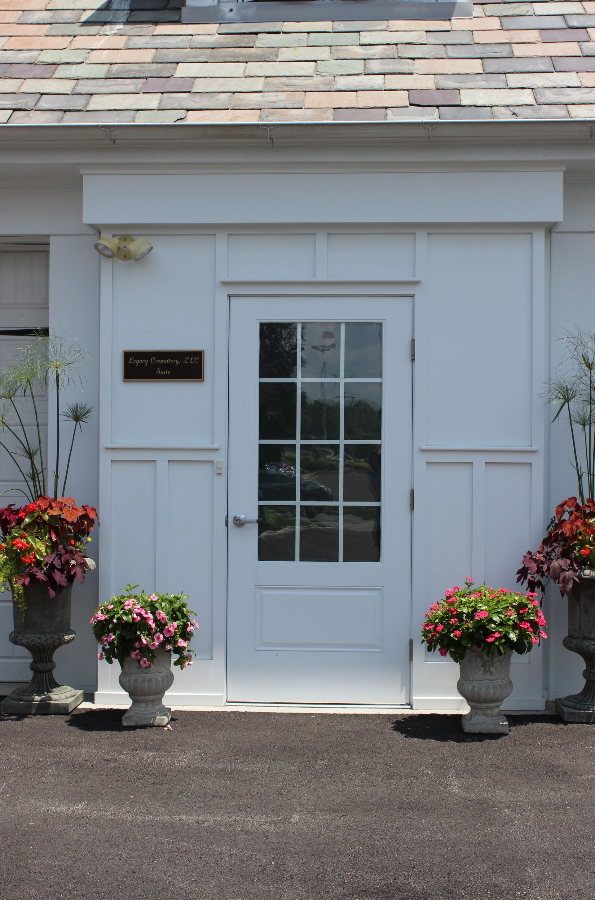 White front entrance with glass door, flanked by potted flowers and a house number plaque.