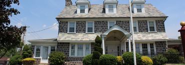 Stone house with a slate roof, white trim, and a landscaped front yard under a clear sky