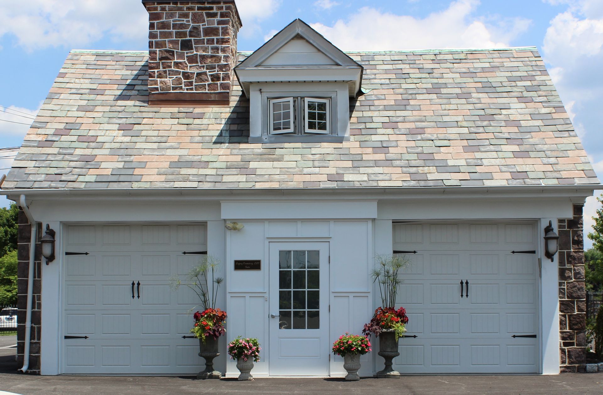 Front view of a white double garage with a shingled roof, central door, and flower pots by the entrance