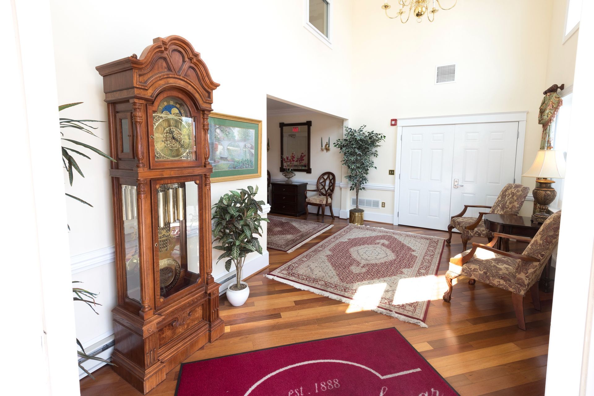 Elegant living room with wooden grandfather clock, patterned rug, potted plant, and white double doors