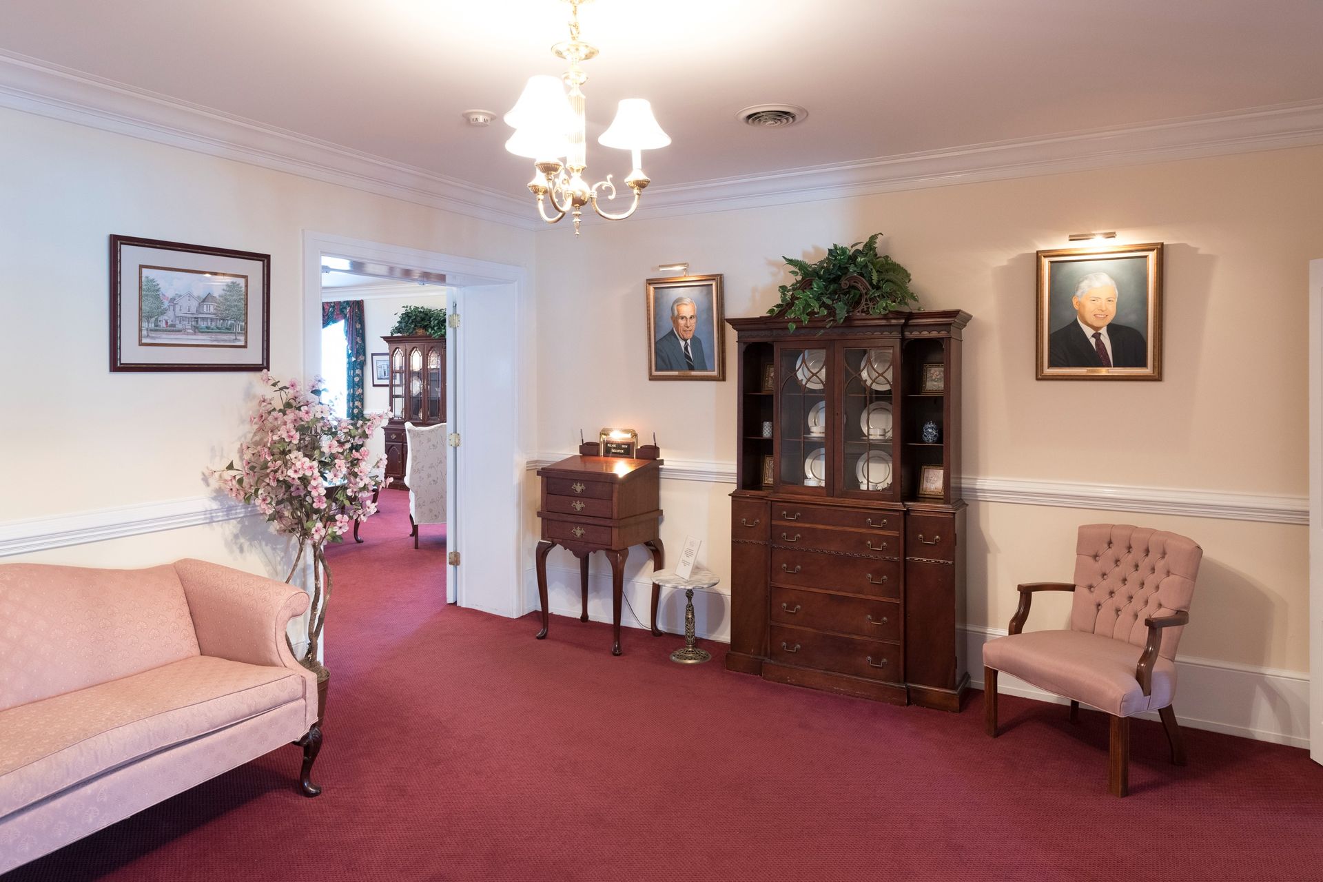 Elegant living room with red carpet, pale sofa, wood cabinet, and floral arrangements.