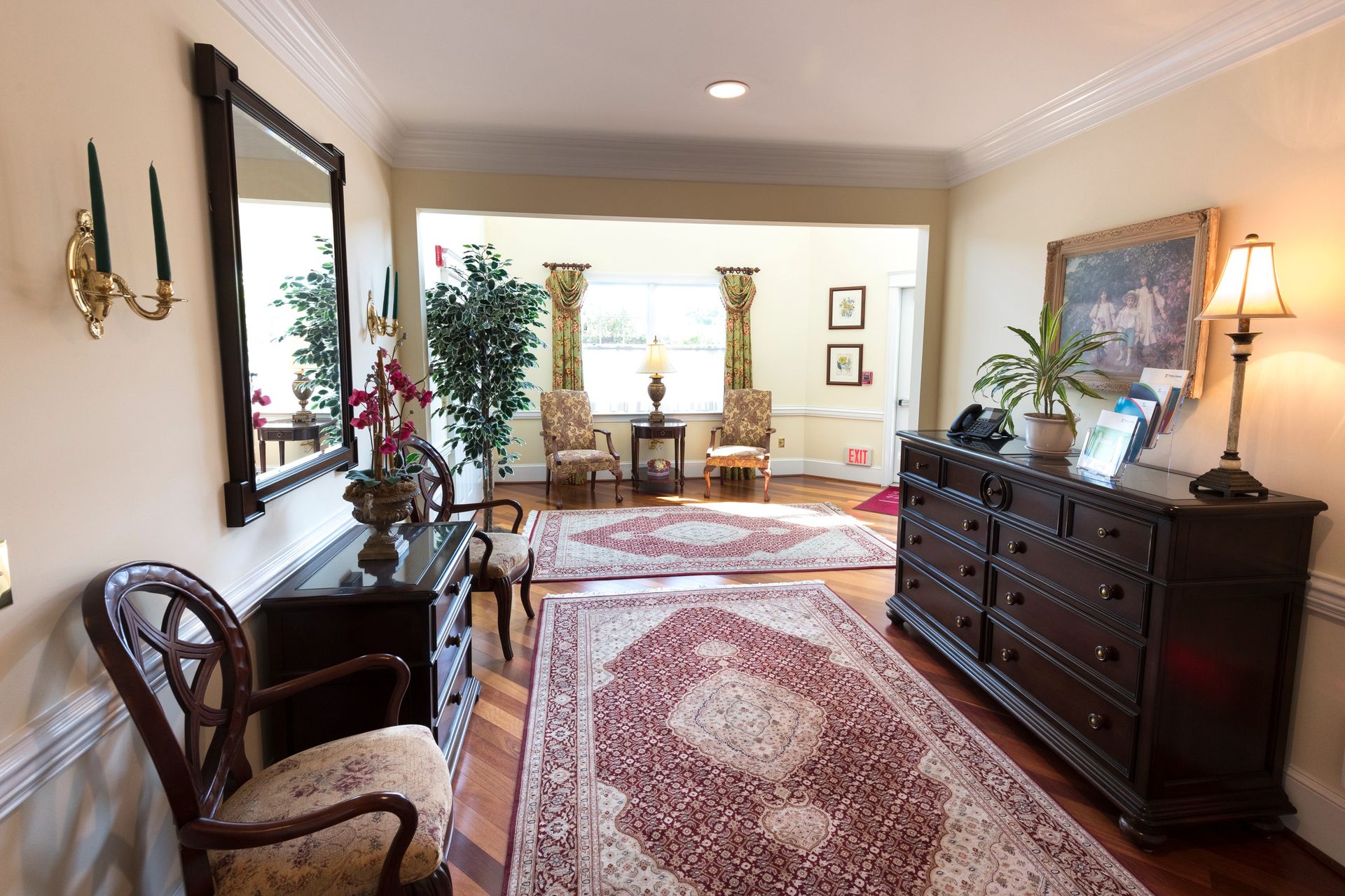 Elegant living room with patterned rug, wooden dresser, chairs, and lamps in warm light