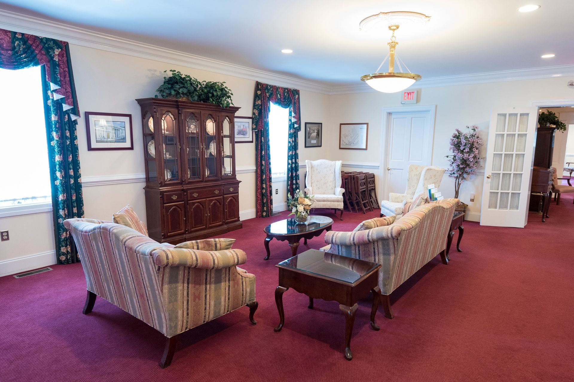 Elegant living room with burgundy carpet, striped sofas, wood cabinet, and large windows with blue curtains