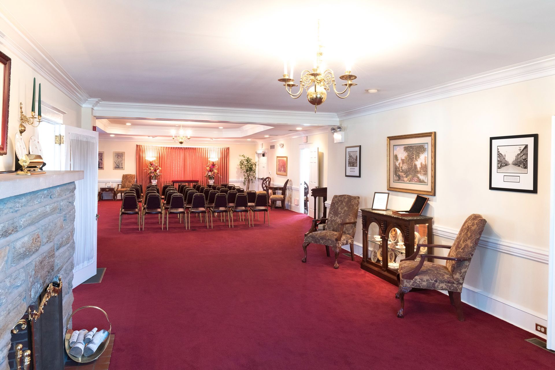 Elegant banquet hall with red carpet, rows of chairs, chandeliers, and framed wall art