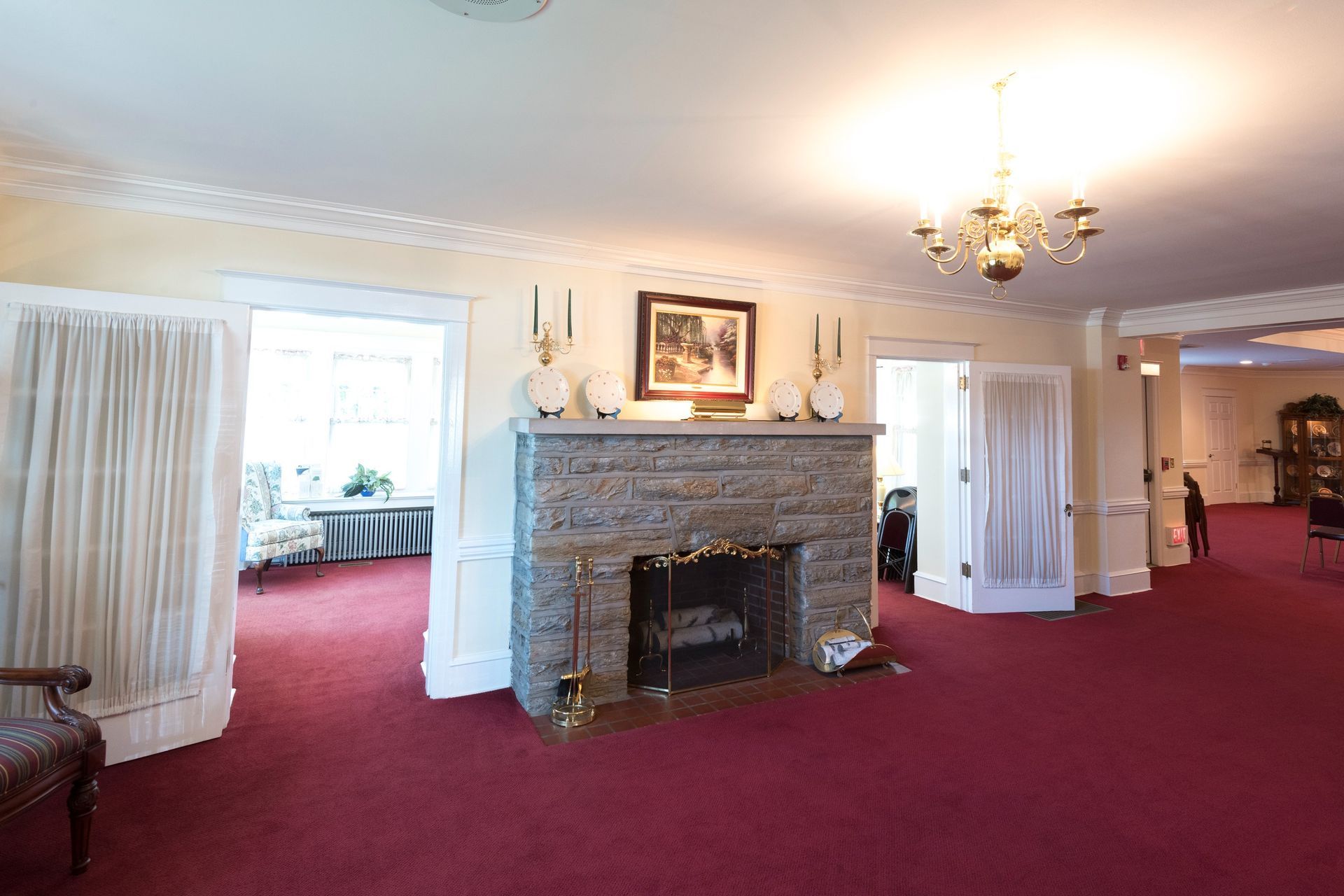Spacious living room with red carpet, white walls, stone fireplace, and curtained doorways