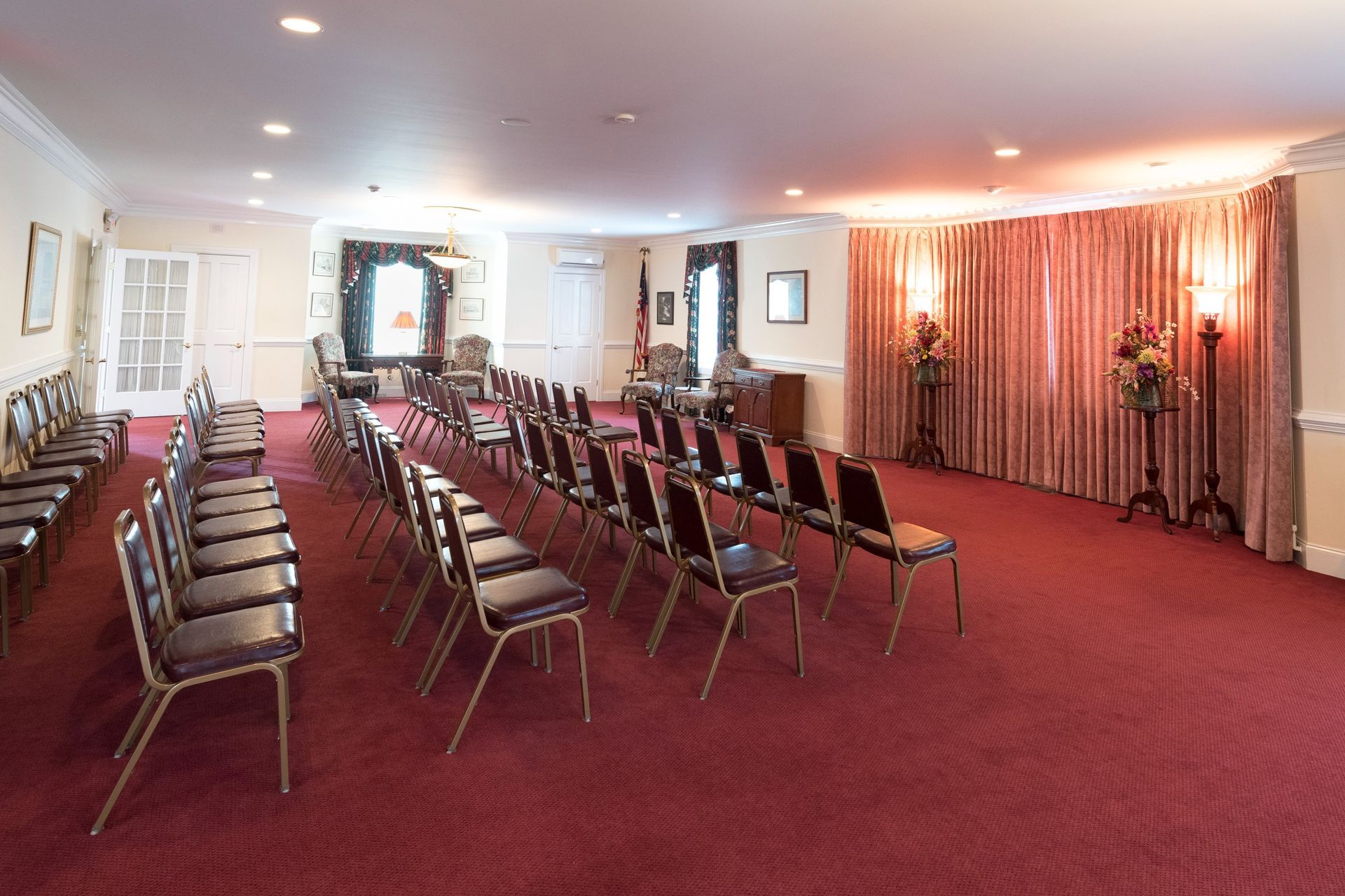 Empty banquet room with rows of chairs on a red carpet and pink curtains