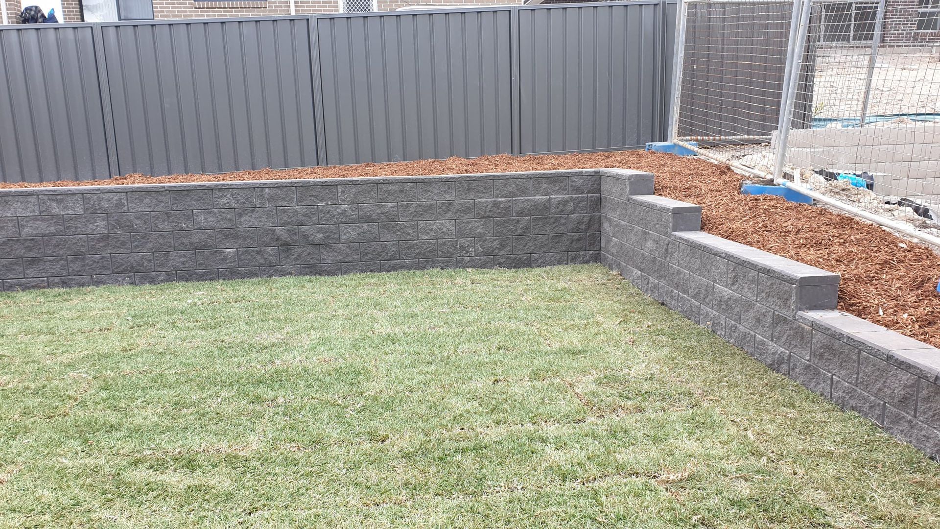 A brick wall surrounds a lush green lawn in a backyard.