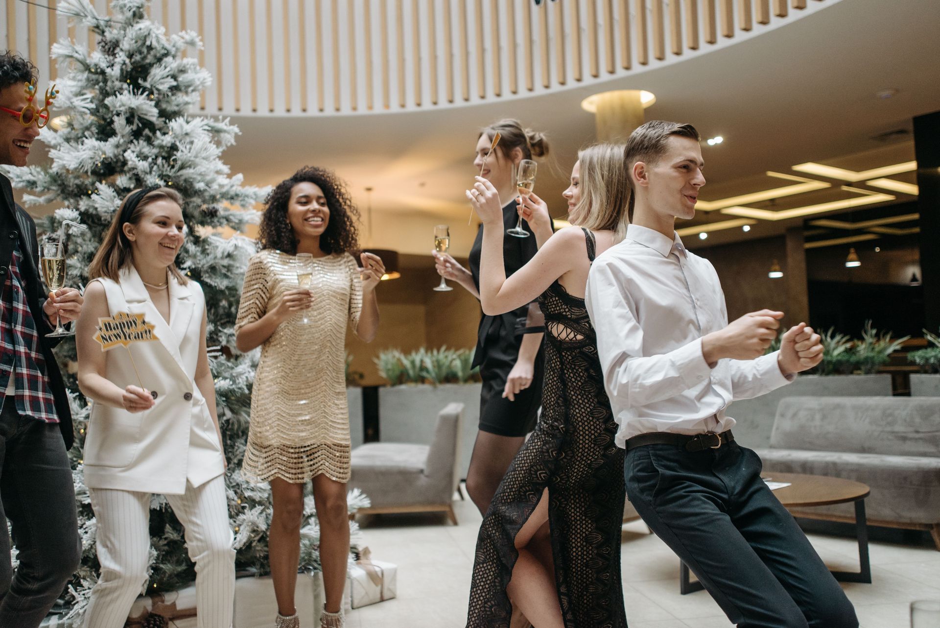 People dancing and socializing in a modern lobby with plants and curved wood ceiling
