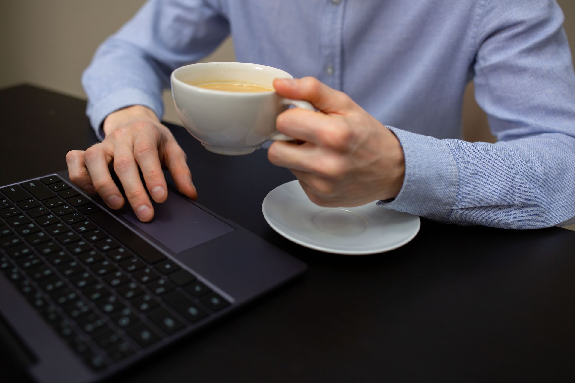 Person using a laptop while holding a white coffee cup at a desk