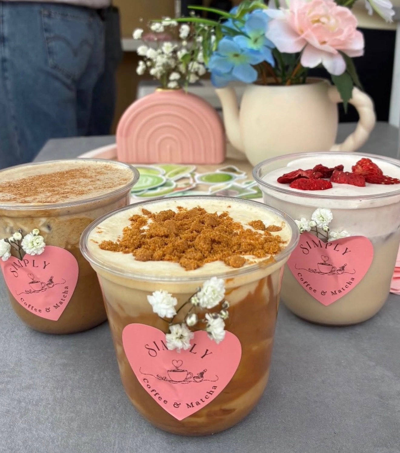 Dessert cups topped with crumbs and strawberries on a table, decorated with pink heart tags and flowers.