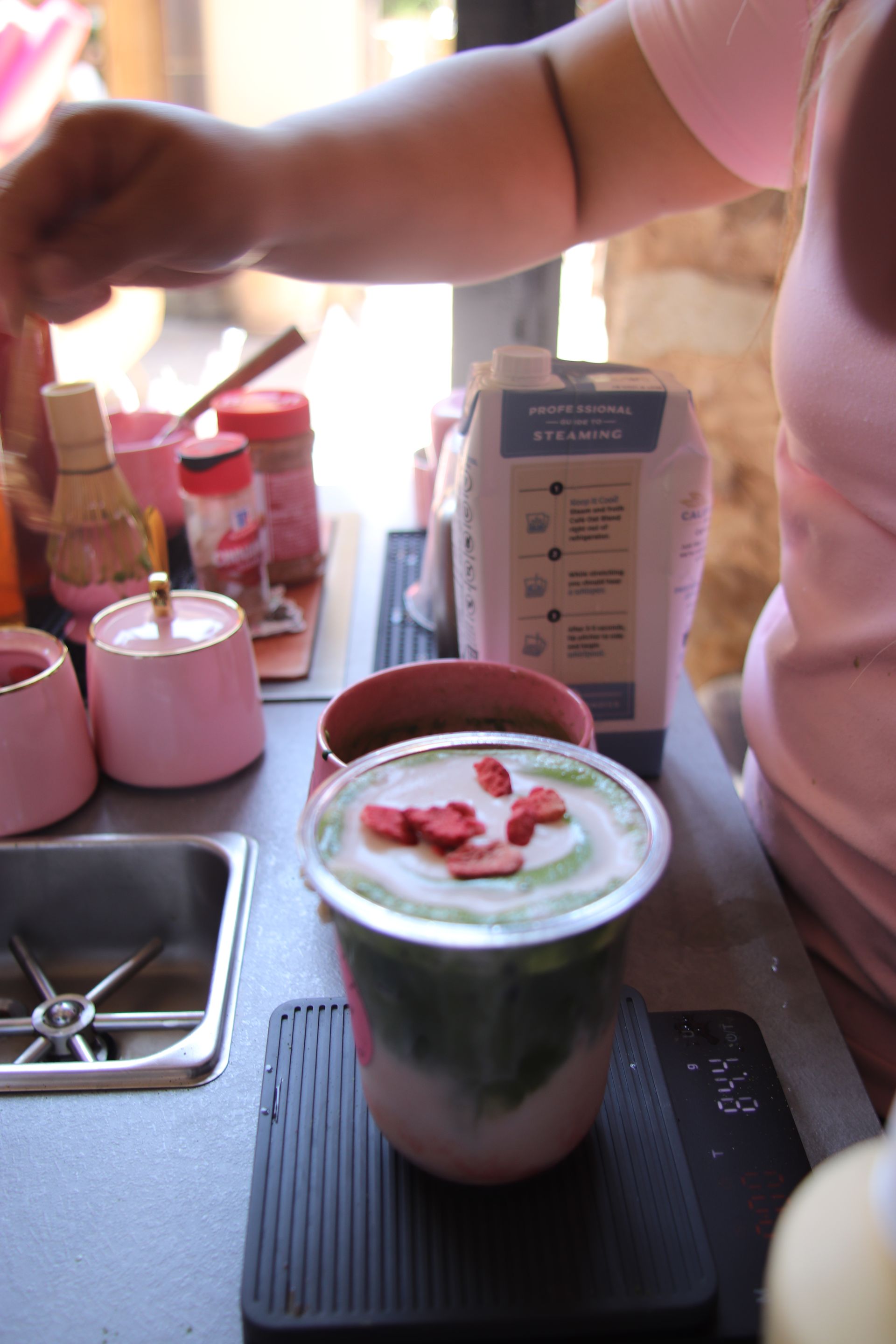 Person pouring a green smoothie topped with strawberries into a glass on a kitchen counter