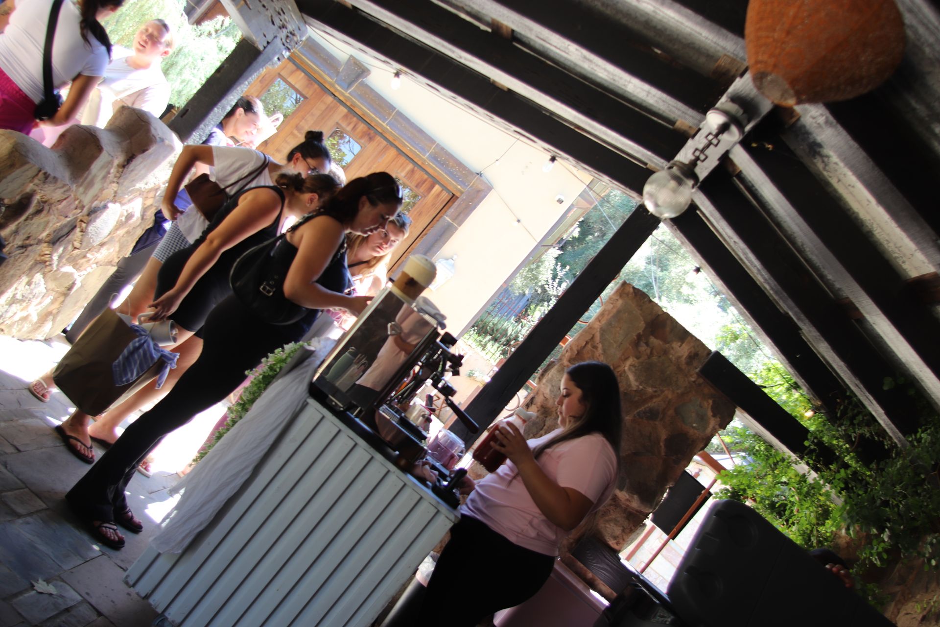 People standing in line at an outdoor counter under a striped canopy, with a woman serving behind it.