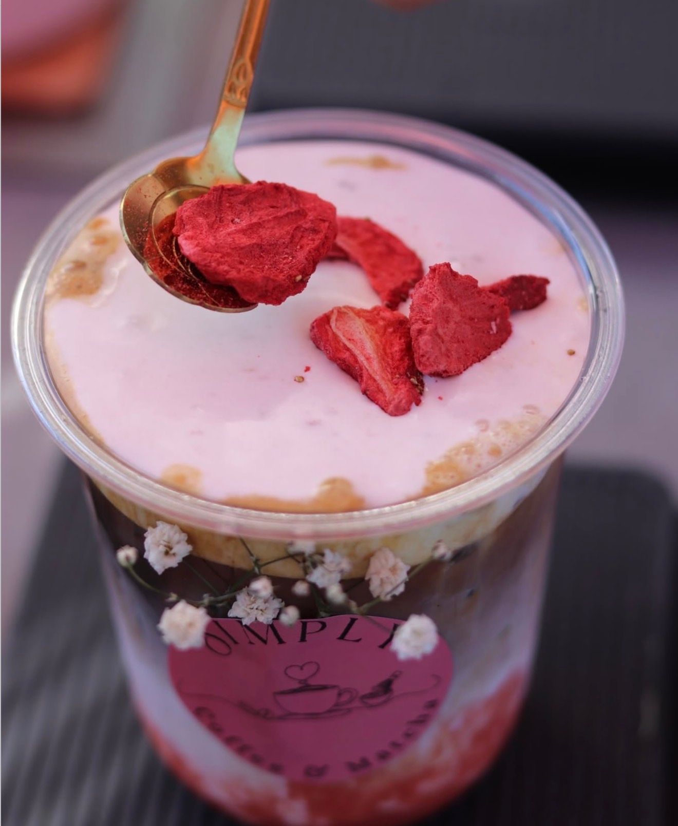 Strawberry dessert in a clear cup with whipped cream and dried strawberry pieces on top, with a spoon.