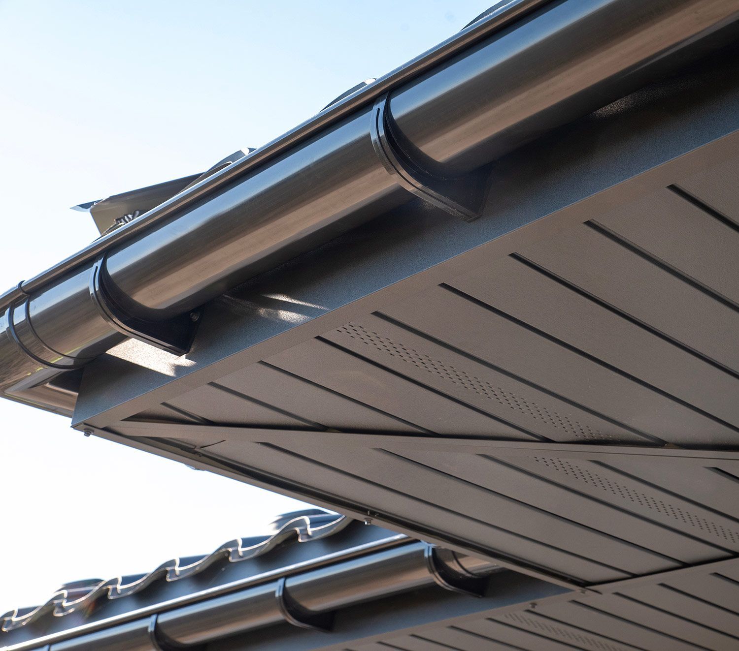 Close-up of black roof gutters and soffit panels on a house against a blue sky