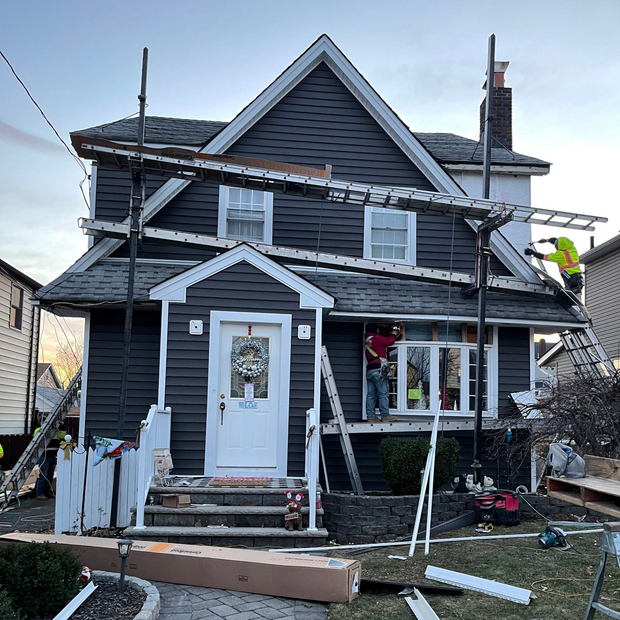 Damaged two-story house with torn siding, debris, and a walkway in front after storm damage
