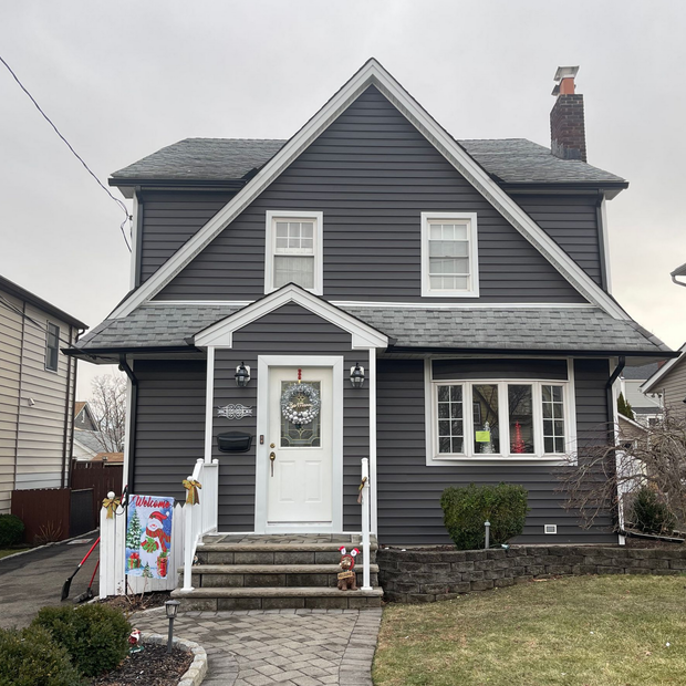 Gray two-story house with white trim, front porch, and small lawn on a cloudy day