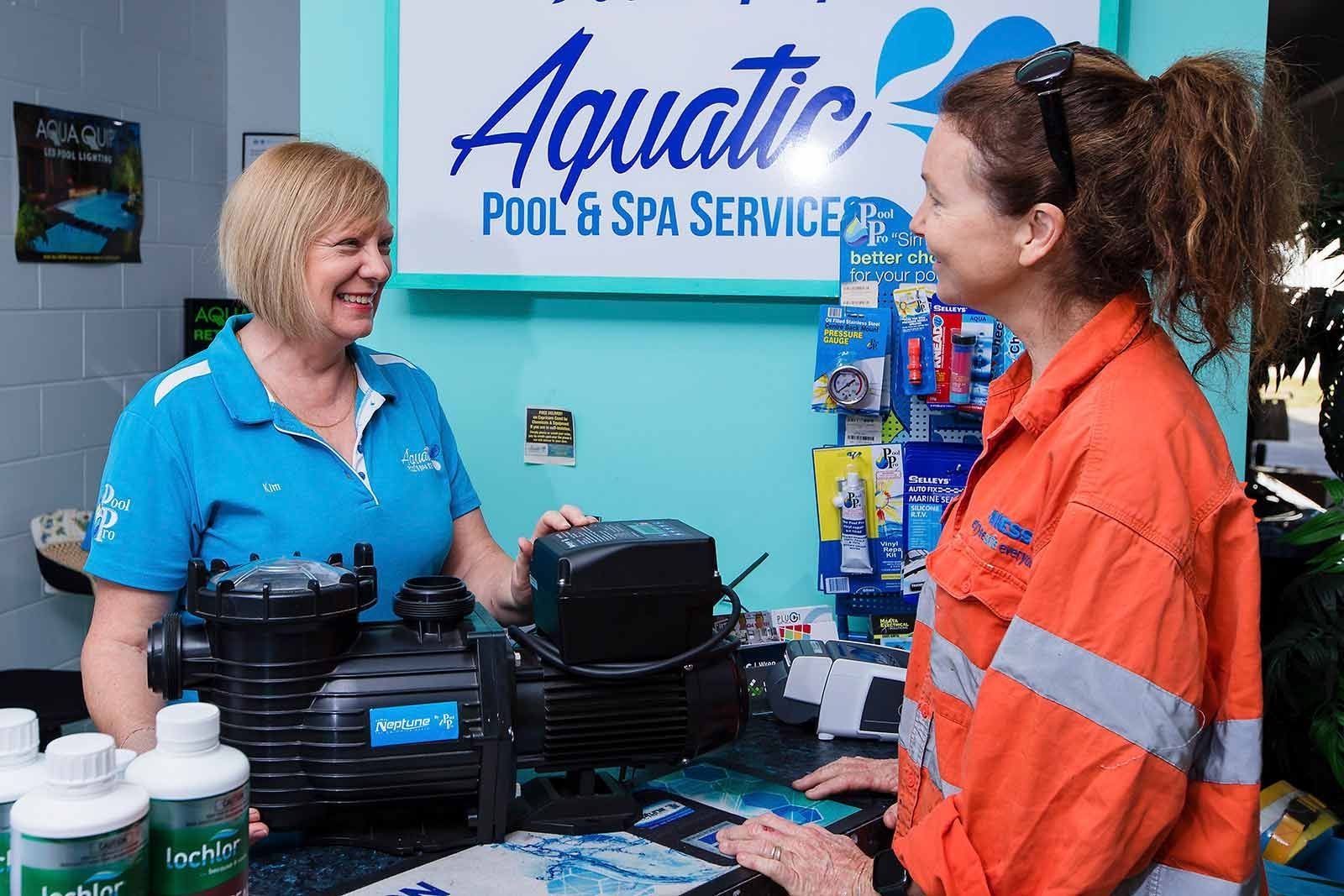 Two Women Are Talking In Front Of A Sign That Says Aquatic Pool & Spa Service — Aquatic Pool & Spa Services In Yeppoon, QLD