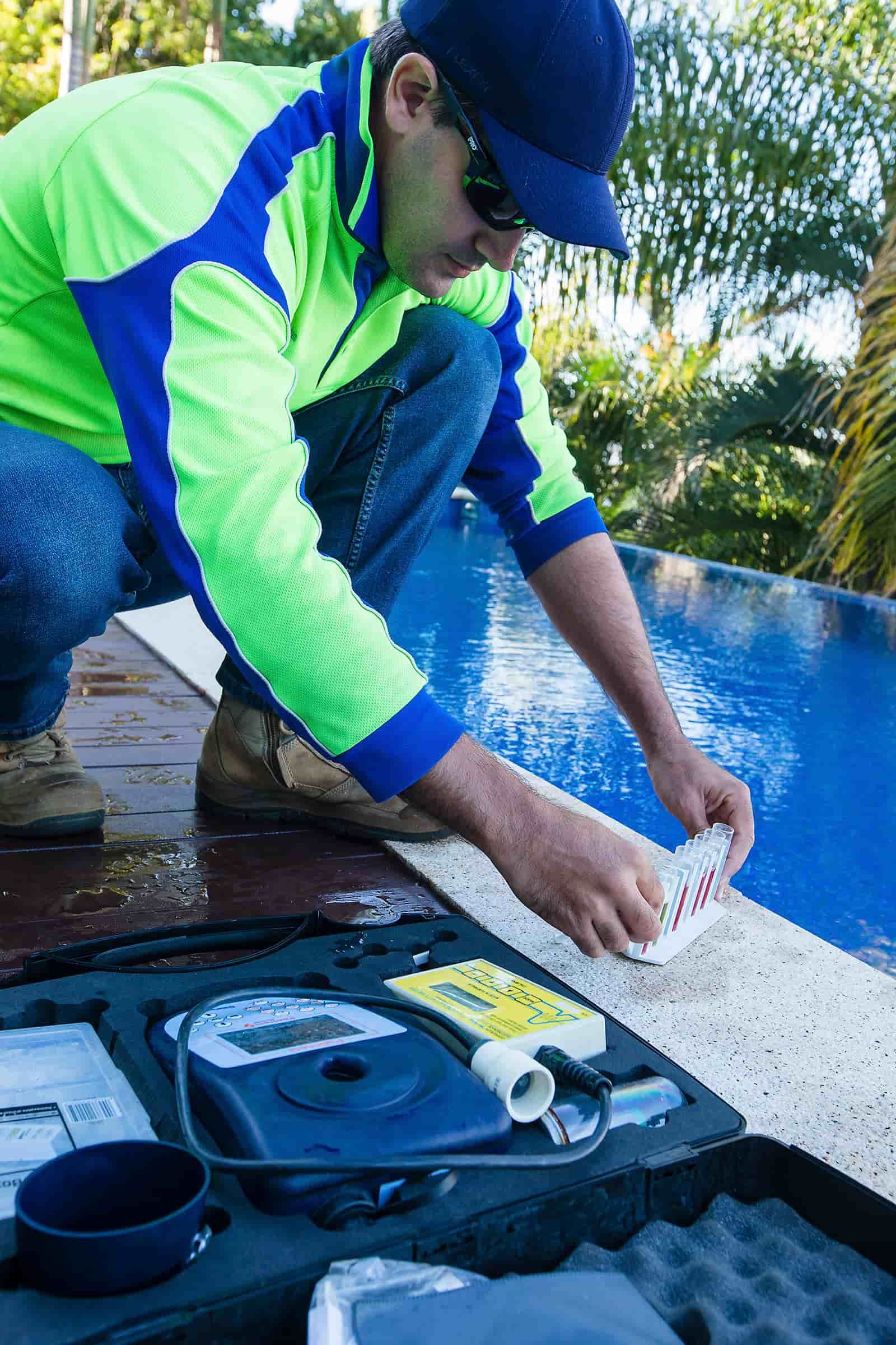A Man Is Kneeling On The Edge Of A Swimming Pool — Aquatic Pool & Spa Services In Capricorn Coast, QLD