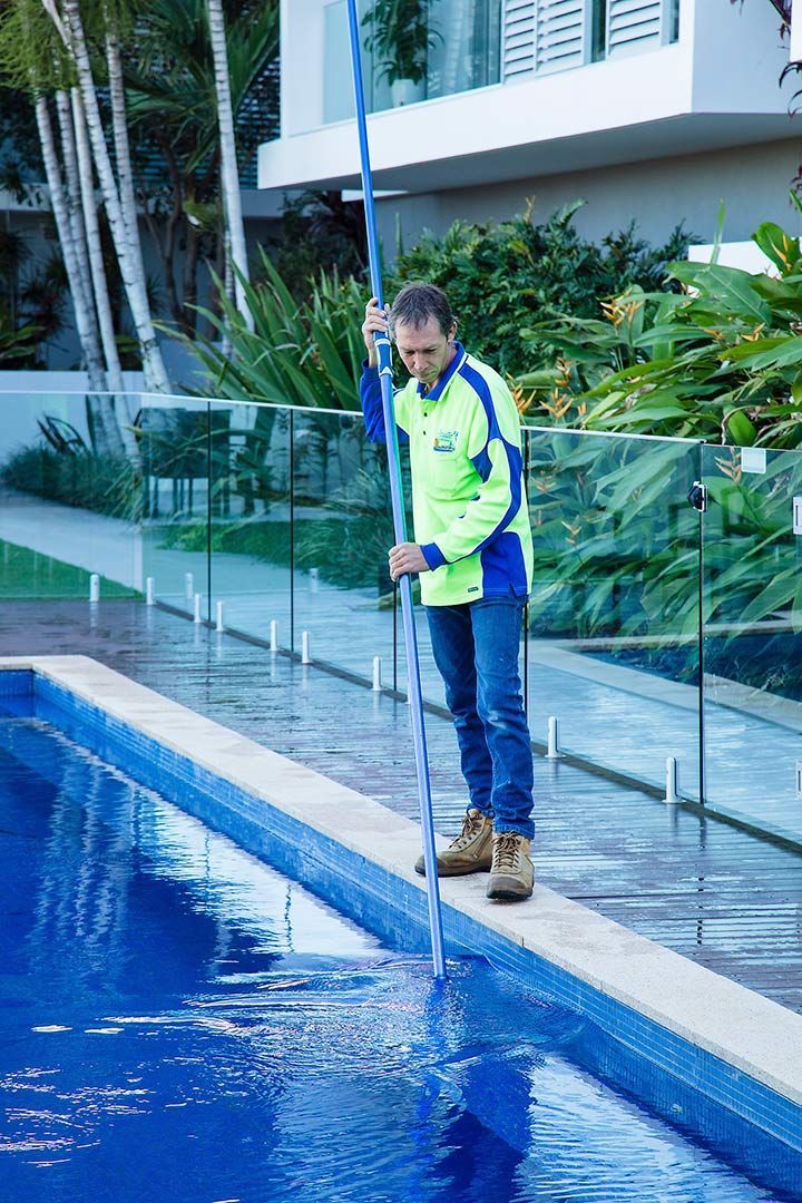 A Man Is Cleaning A Swimming Pool With A Mop — Aquatic Pool & Spa Services In Capricorn Coast, QLD