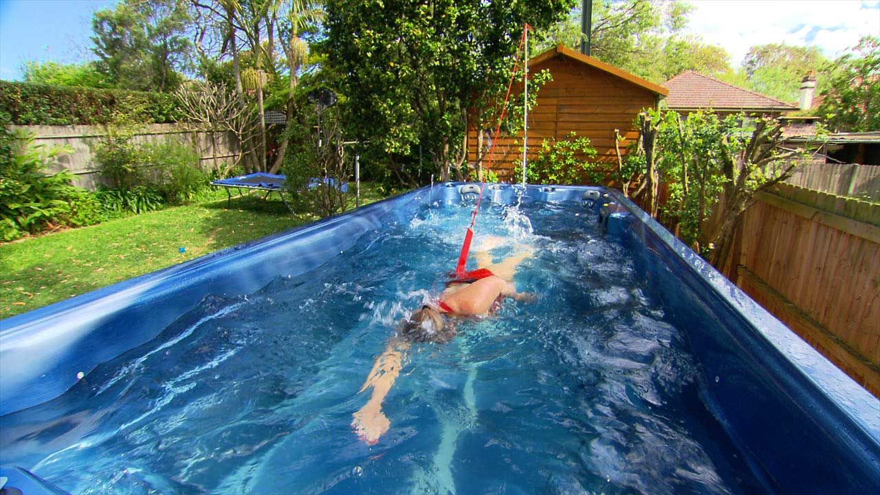 A Person Is Swimming In A Large Swimming Pool In A Backyard — Aquatic Pool & Spa Services In Yeppoon, QLD