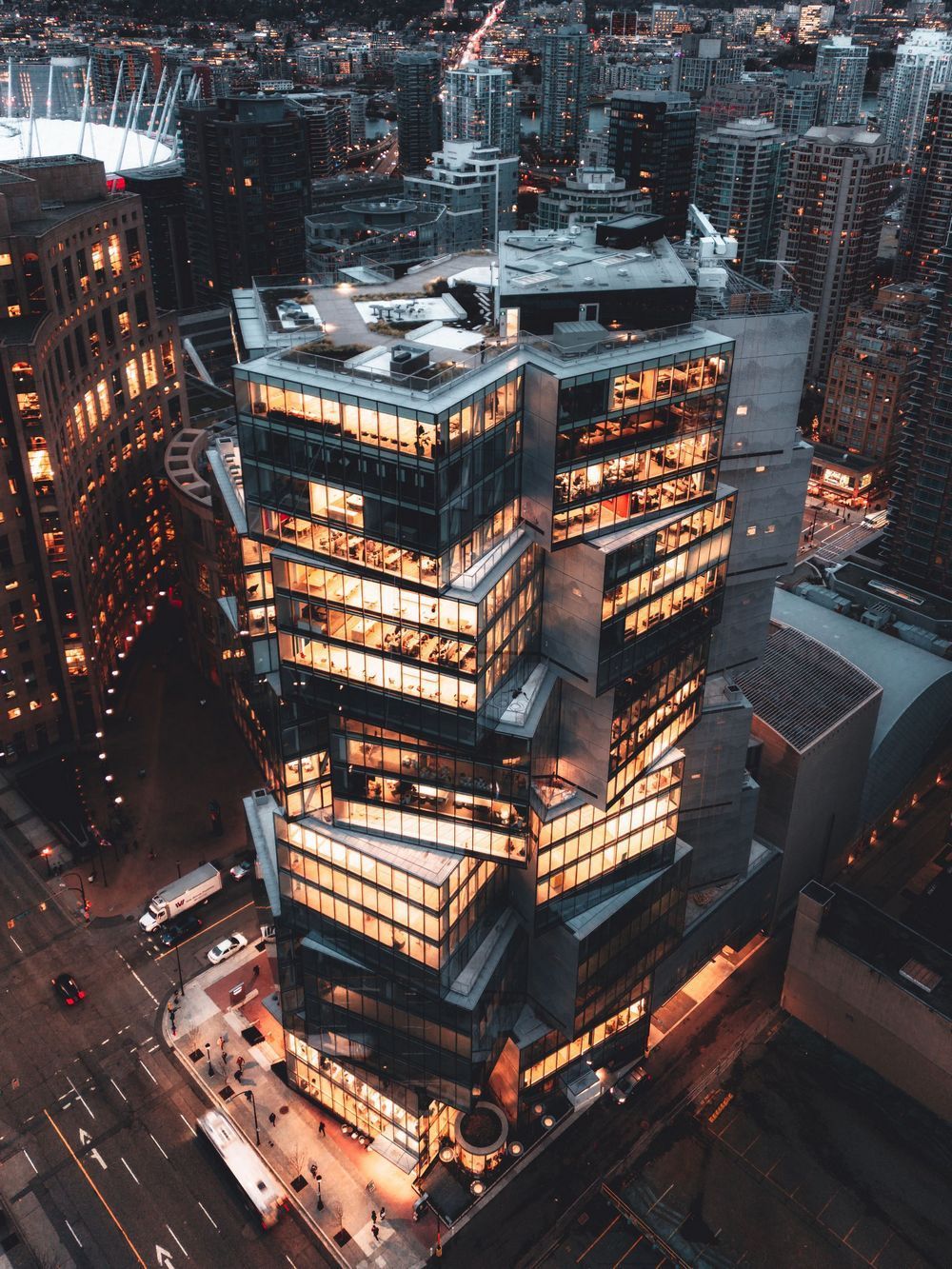 Aerial view of a lit modern skyscraper at night in a dense city downtown.