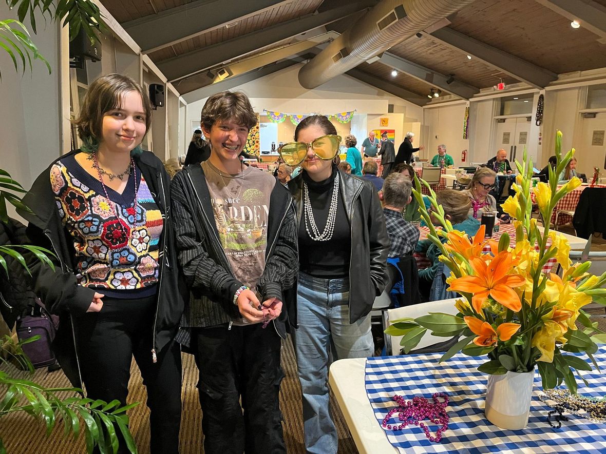 Three people pose at an indoor event beside a table with a flower arrangement.