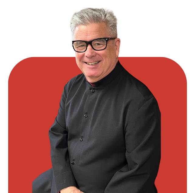 Smiling man in black shirt and glasses seated before a red background