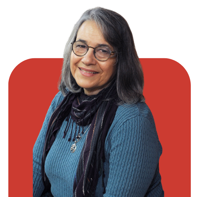 Portrait of a smiling person with glasses, gray hair, and a blue sweater on a red background