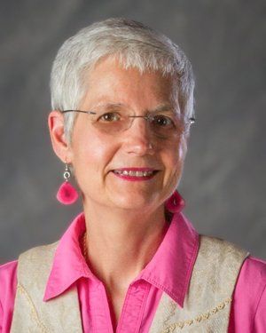 a woman wearing glasses and a pink shirt is smiling for the camera .