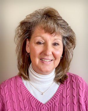 a woman in a pink sweater and white turtleneck is smiling for the camera .