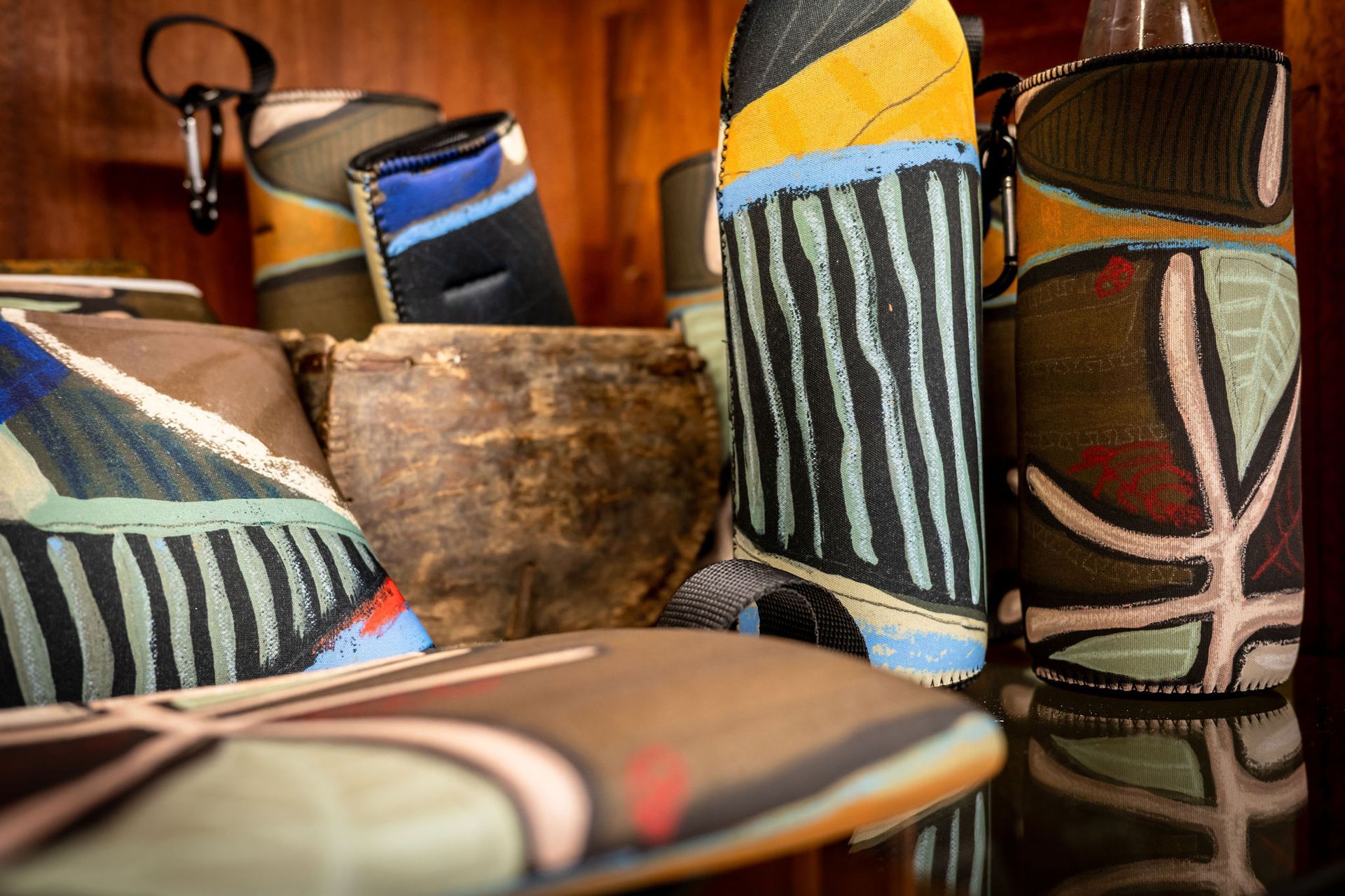 Colorful, patterned fabric sleeves for bottles and accessories arranged on a shelf with a wooden bowl.