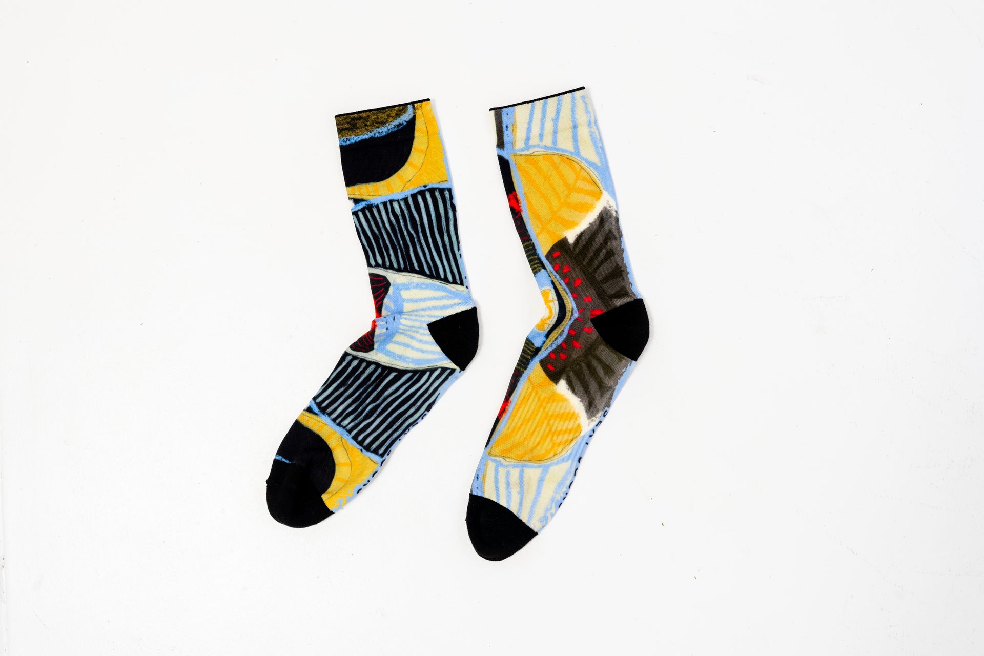 Two crew socks with an abstract, geometric pattern in yellow, light blue, dark grey, and black on a white background.