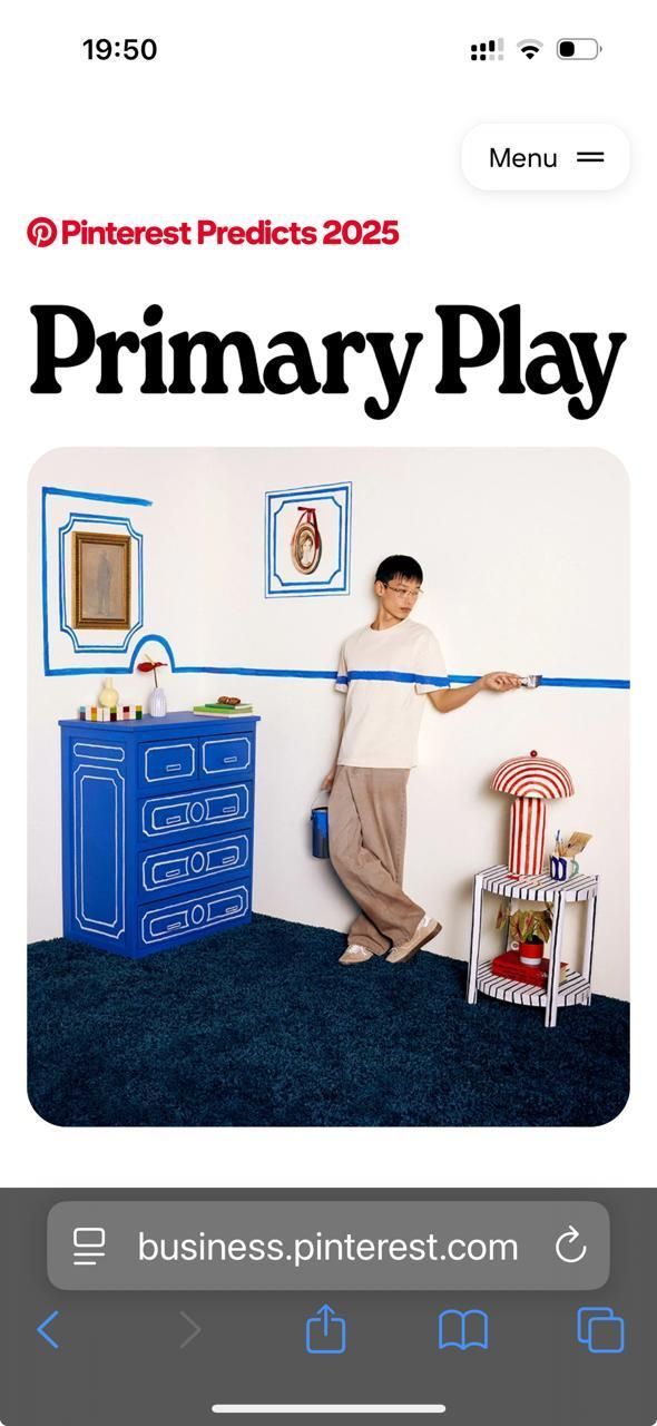 A person leans against a white wall decorated with blue tape outlines, a blue dresser, and a red-and-white striped lamp.