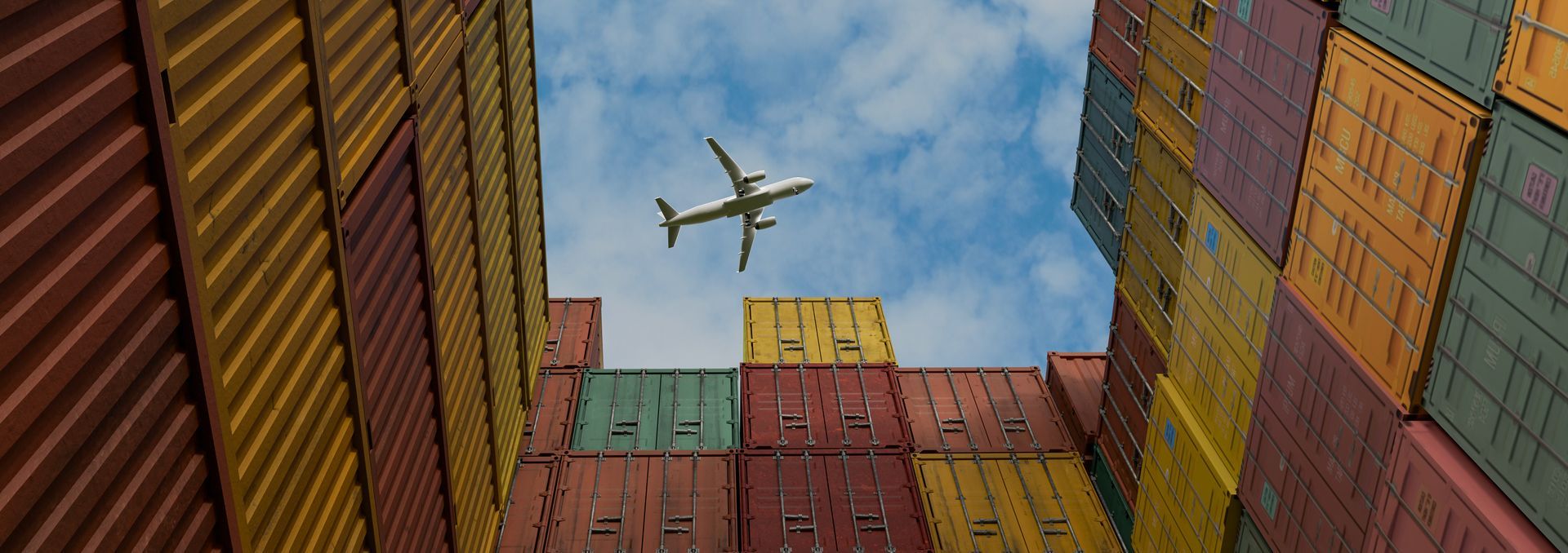 View of a plane in the air, seen through a lot of colorful shipping containers.