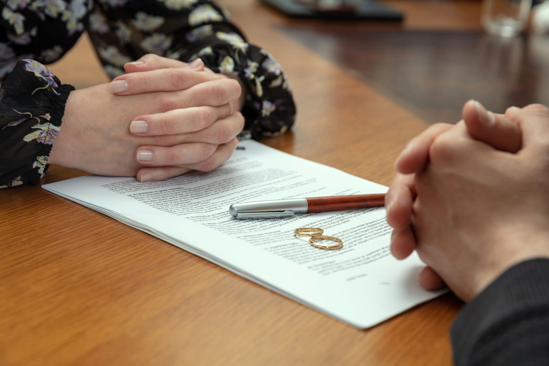A man and a woman are sitting at a table with their hands folded over a piece of paper. A man and a woman are sitting at a table with their hands folded over a piece of paper.