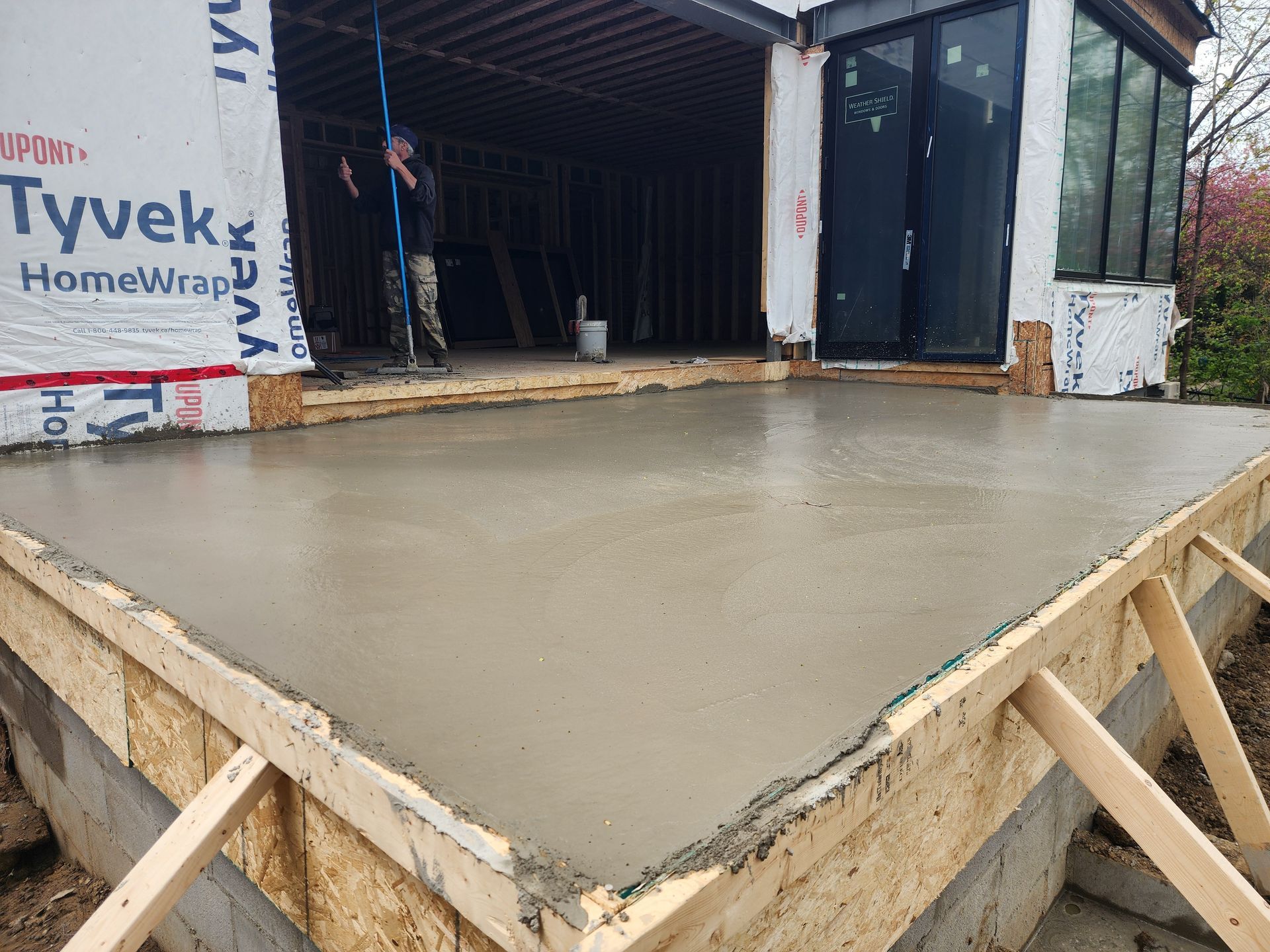 Freshly poured concrete slab at a house under construction, with wood forms and Tyvek-wrapped walls.