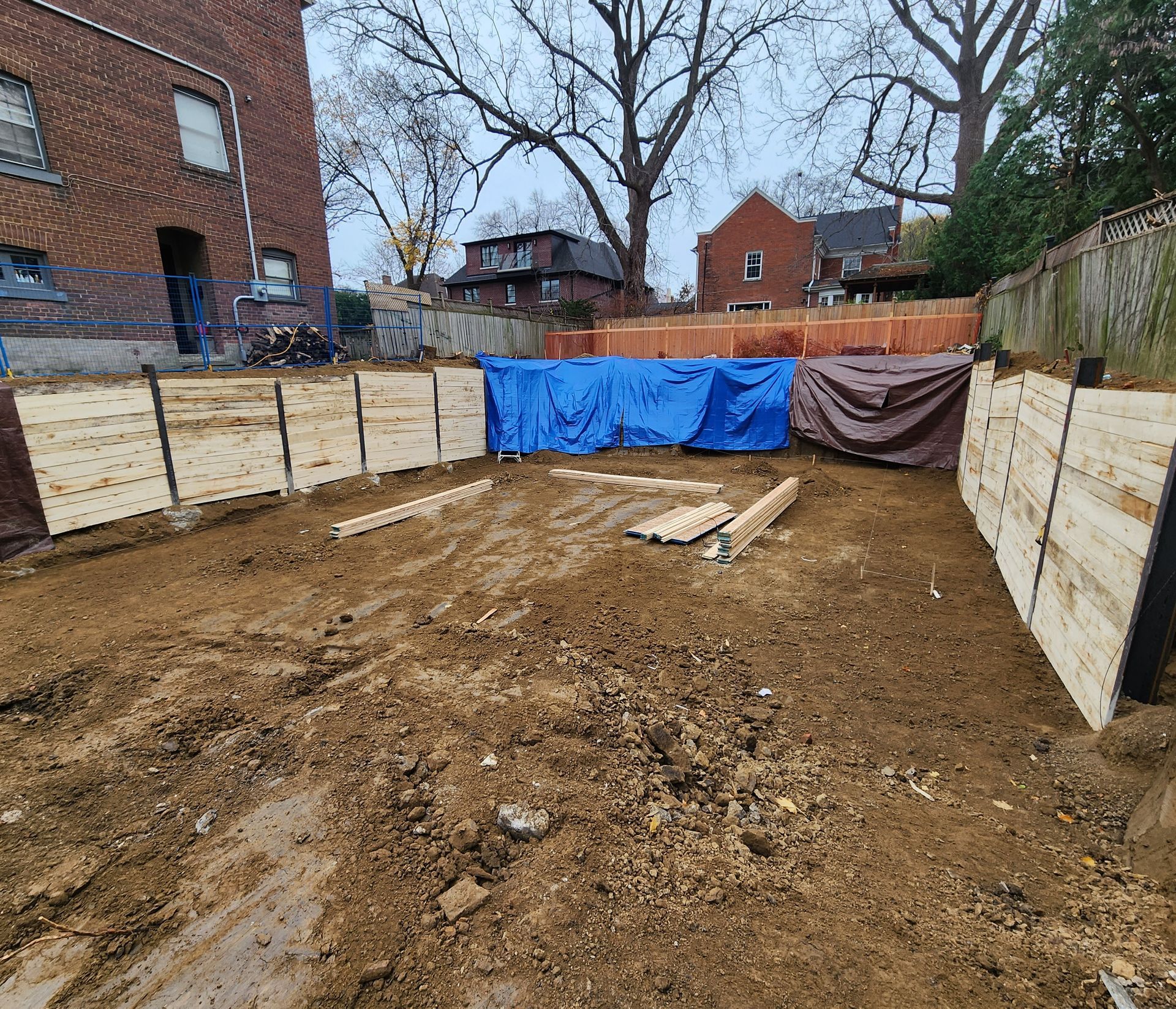 Empty dirt lot enclosed by plywood fencing, with blue and brown tarps at the far end.