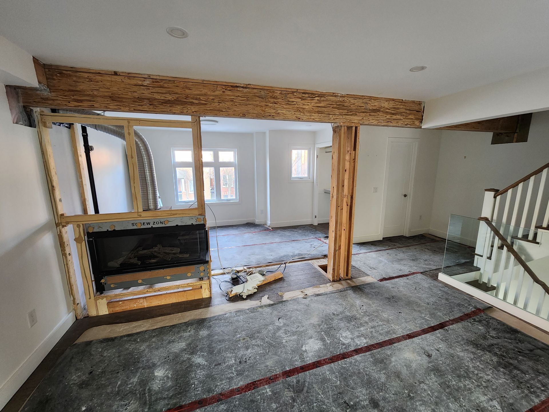 Interior view of a room under construction with exposed wooden beams, fireplace frame, and stairway.