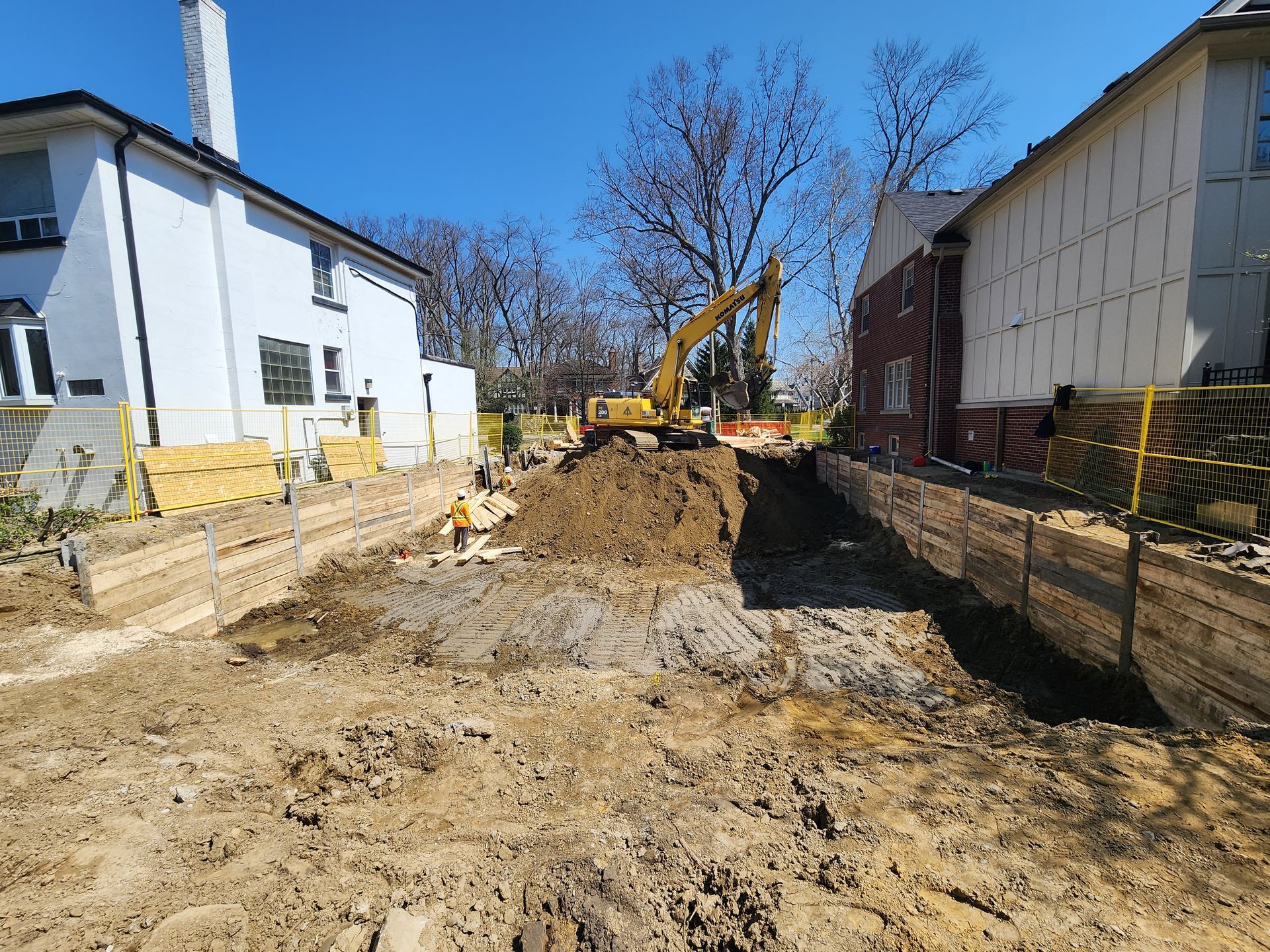 A yellow excavator is digging a hole in the dirt in front of a house.