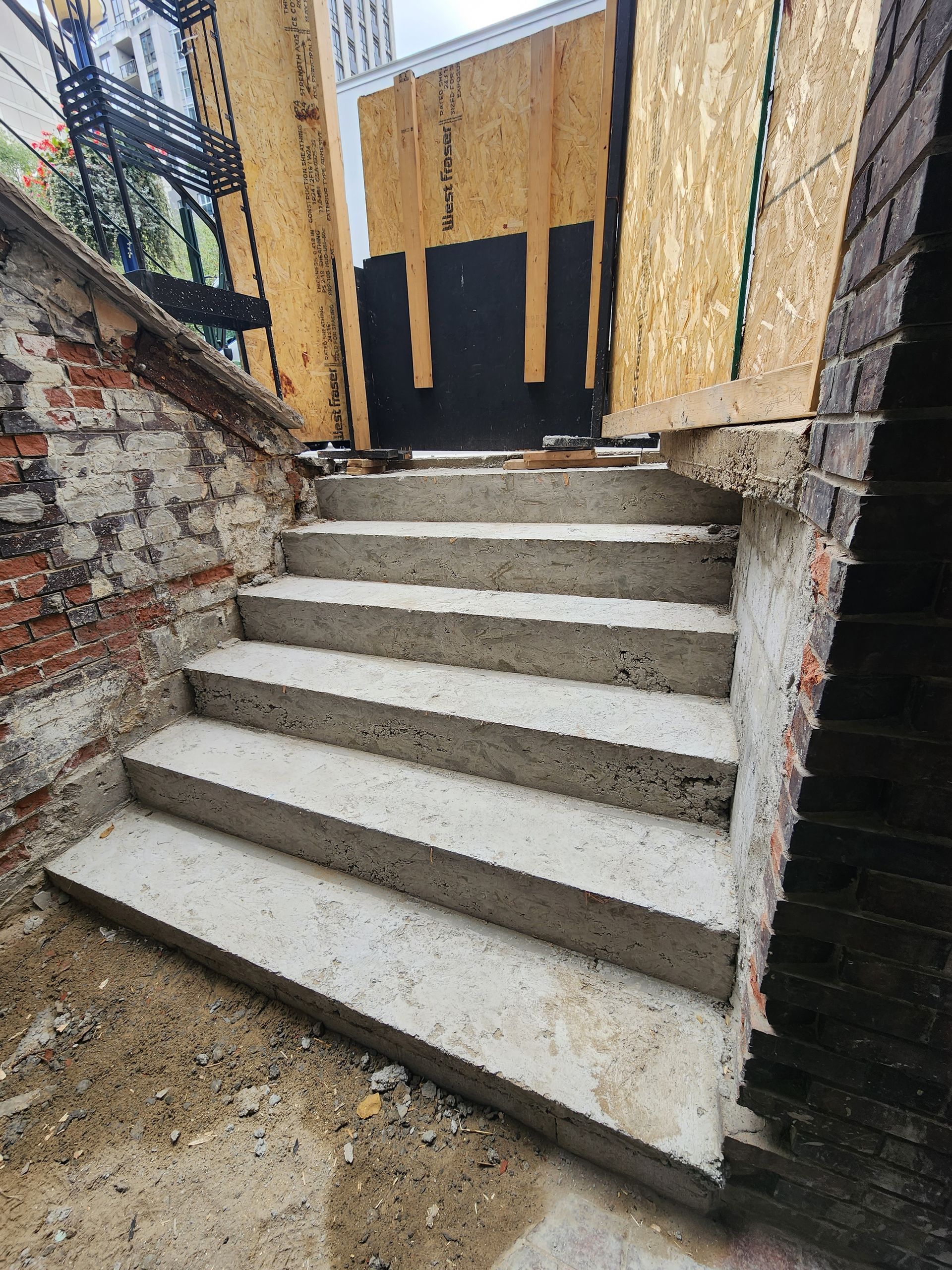 Concrete steps leading up to a doorway; brick and plywood walls.