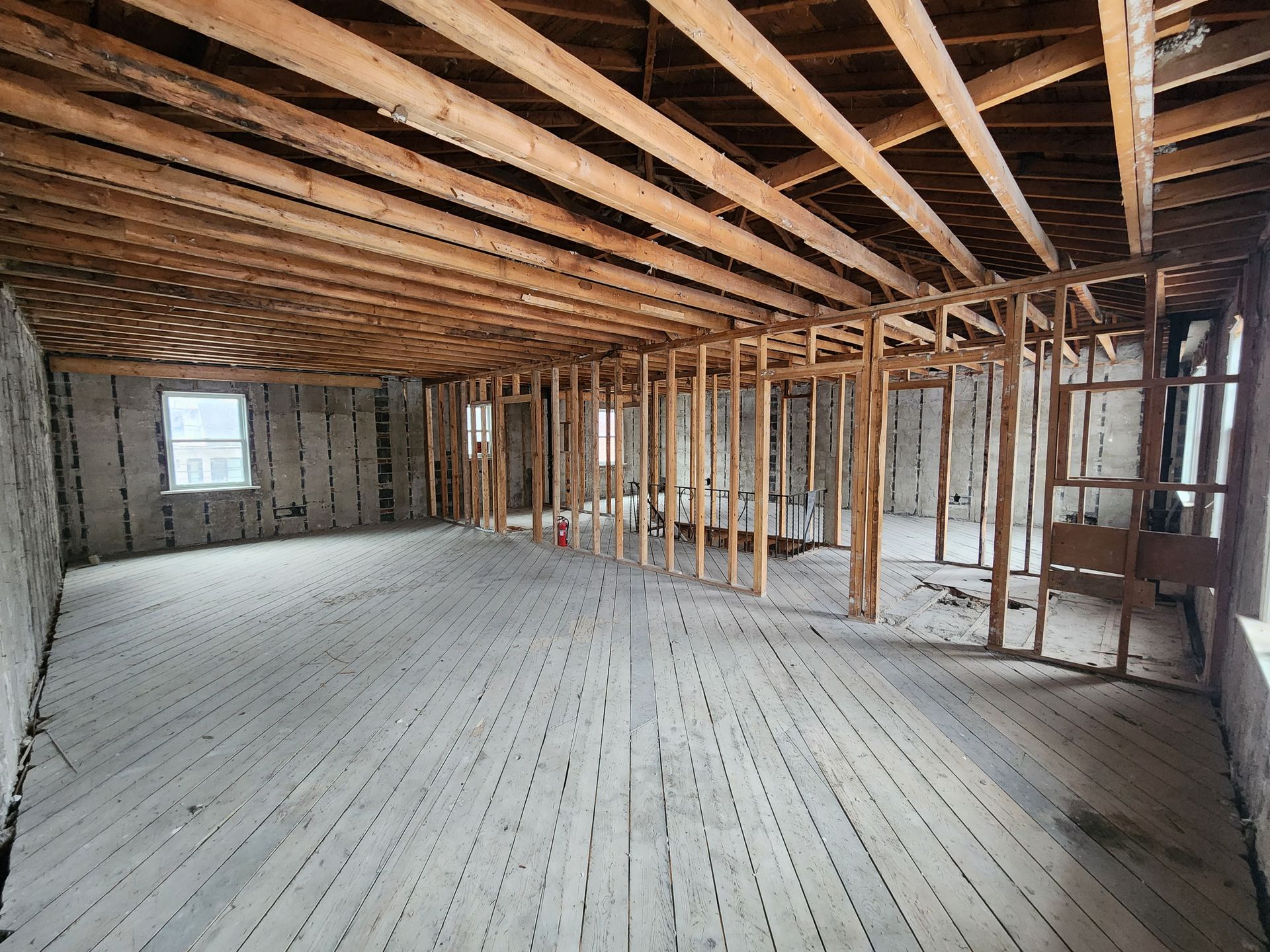 Interior of a room undergoing renovation; wooden floorboards, exposed ceiling beams, and stud walls.