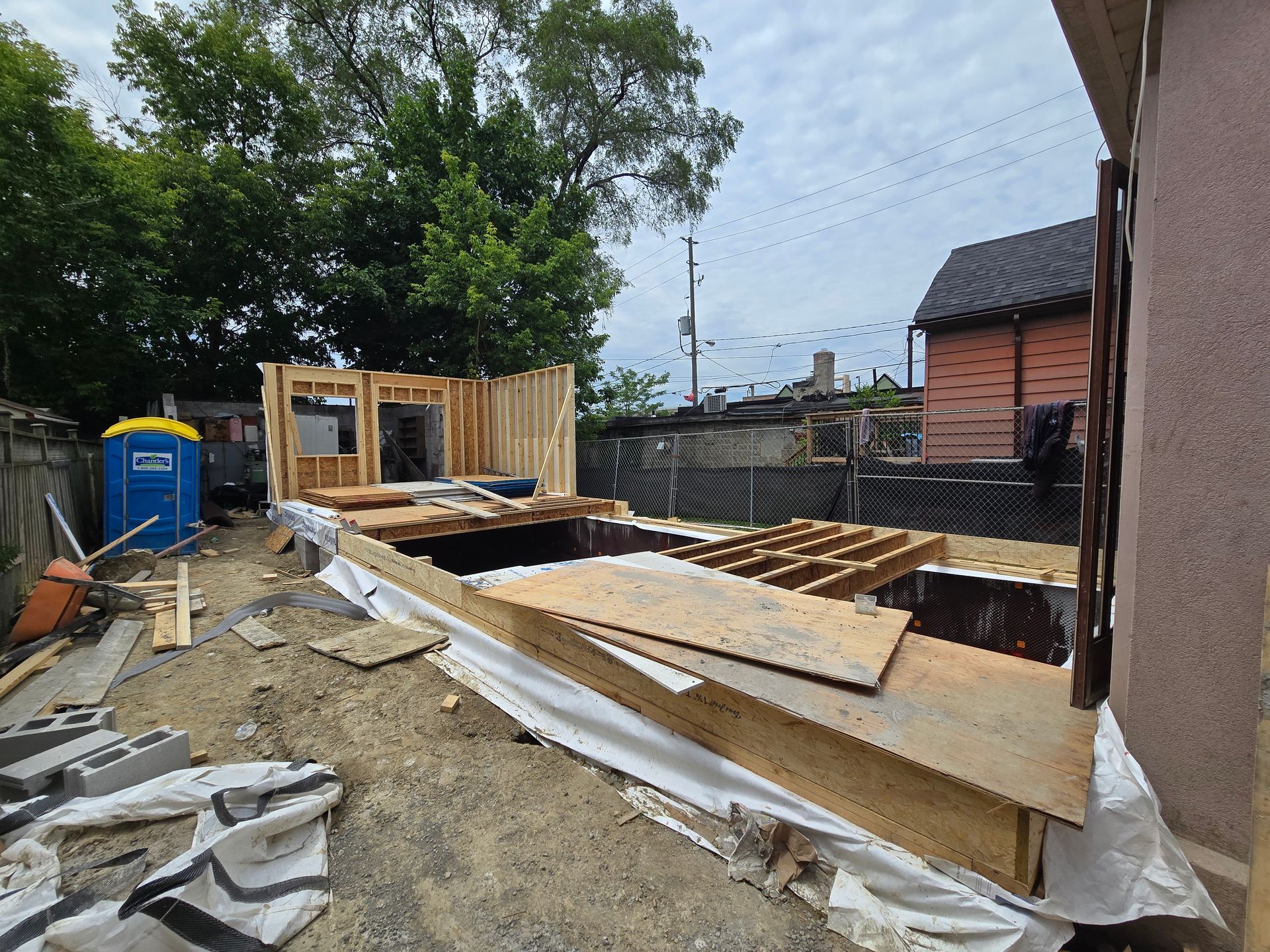 A house under construction with a blue portable toilet in the background.