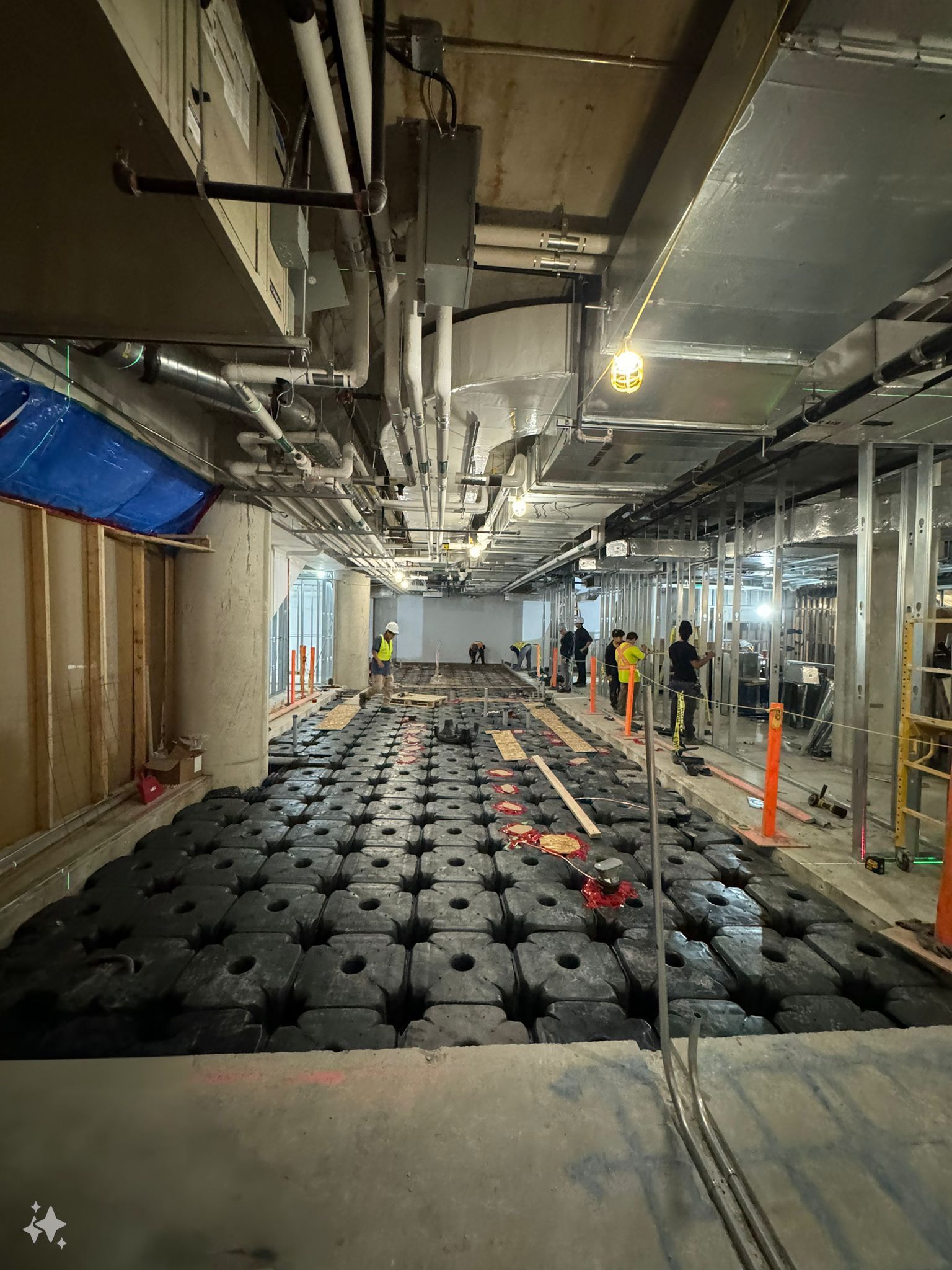 Construction site: Raised flooring installation in a long hallway, workers present, exposed utilities overhead.