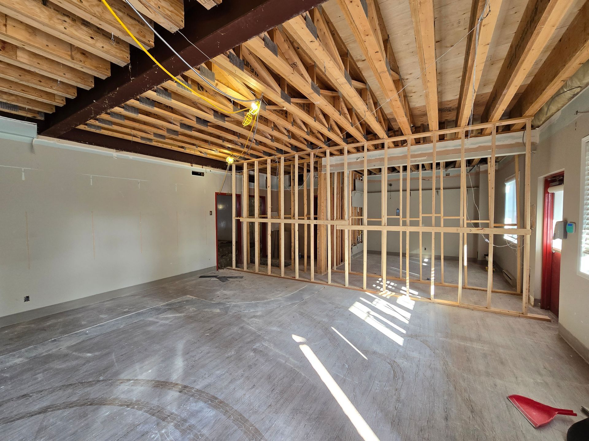 Interior view of a room under construction with exposed wooden beams, studs, and concrete floor.