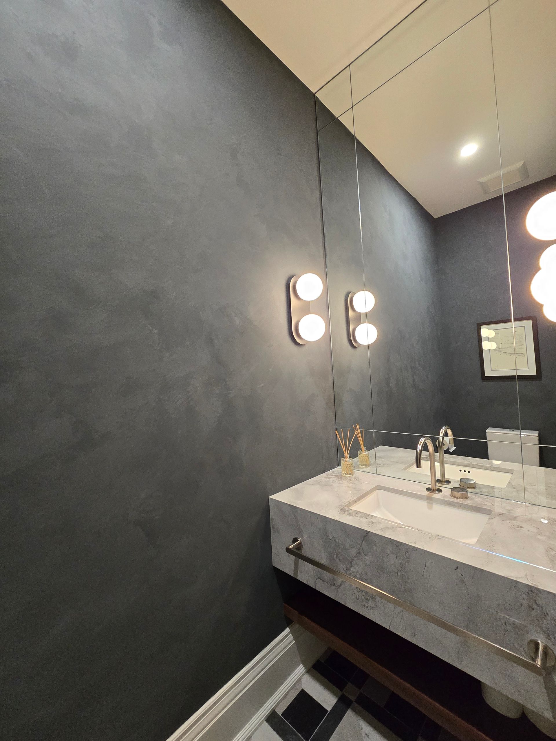 Dark bathroom with marble sink, metallic fixtures, and wall sconces.