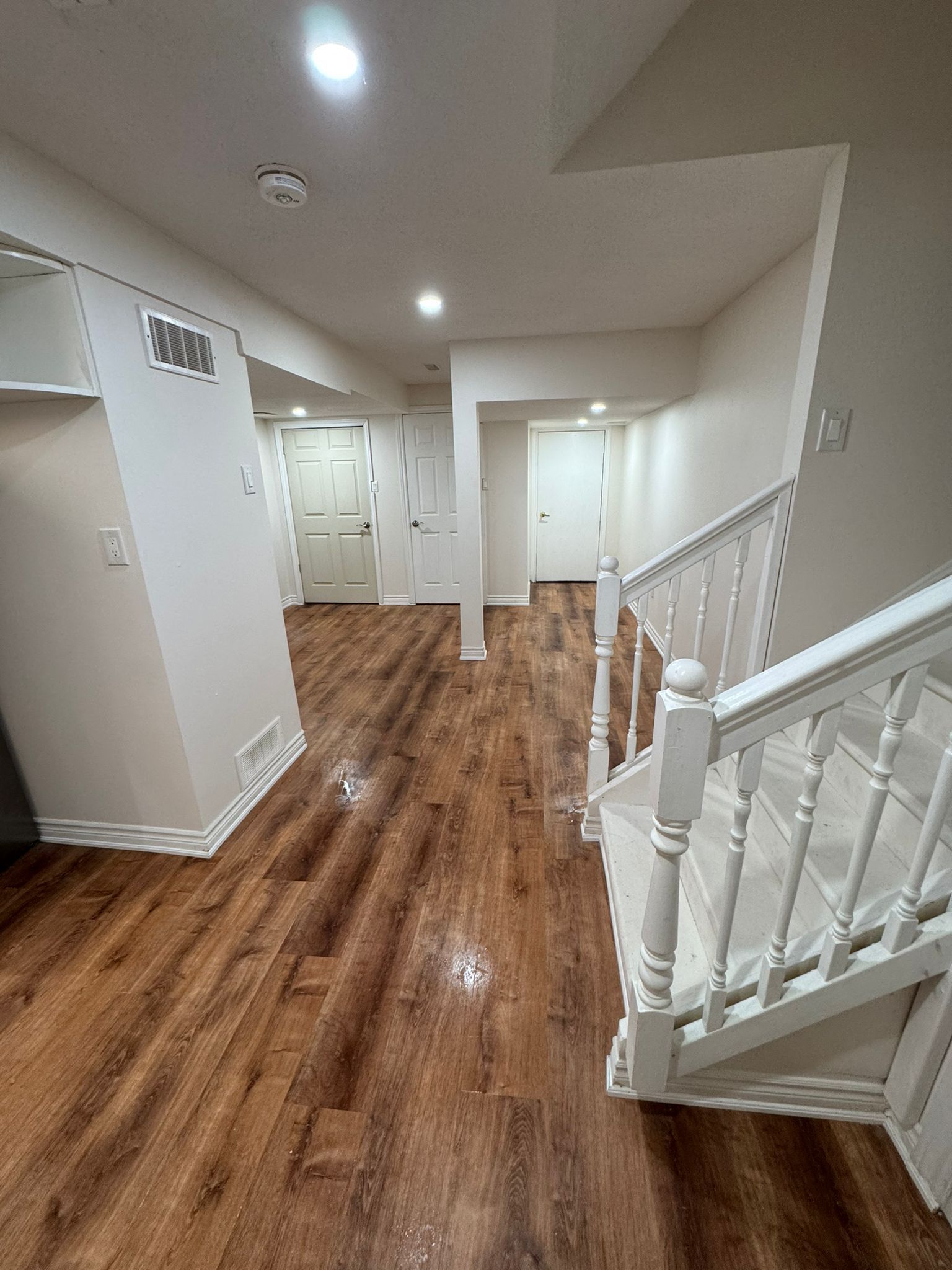 Bright hallway with wood floors, white walls, and a white staircase railing on the right.