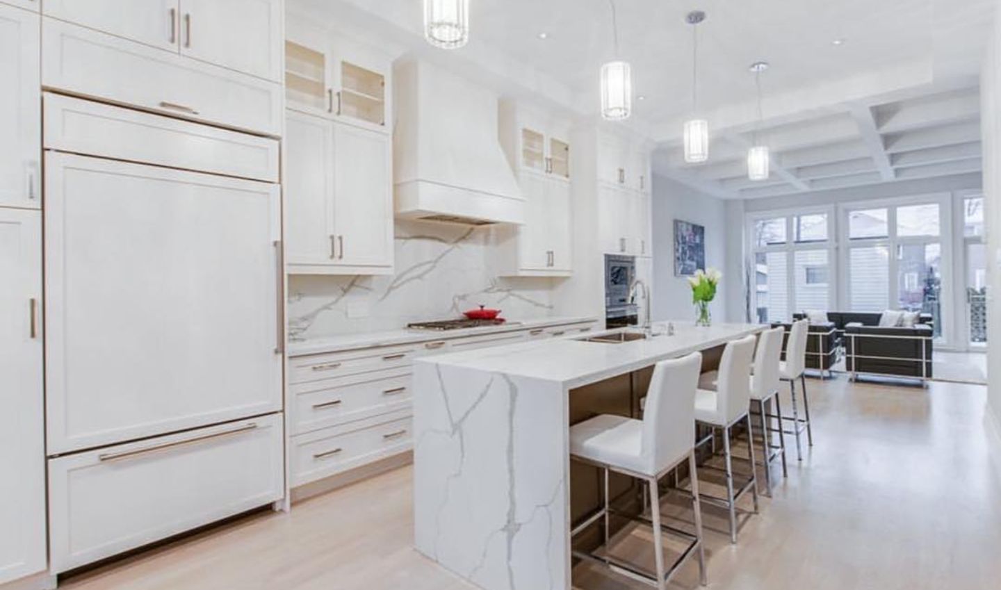 Bright white modern kitchen with marble island, bar stools, and large windows in an open living space