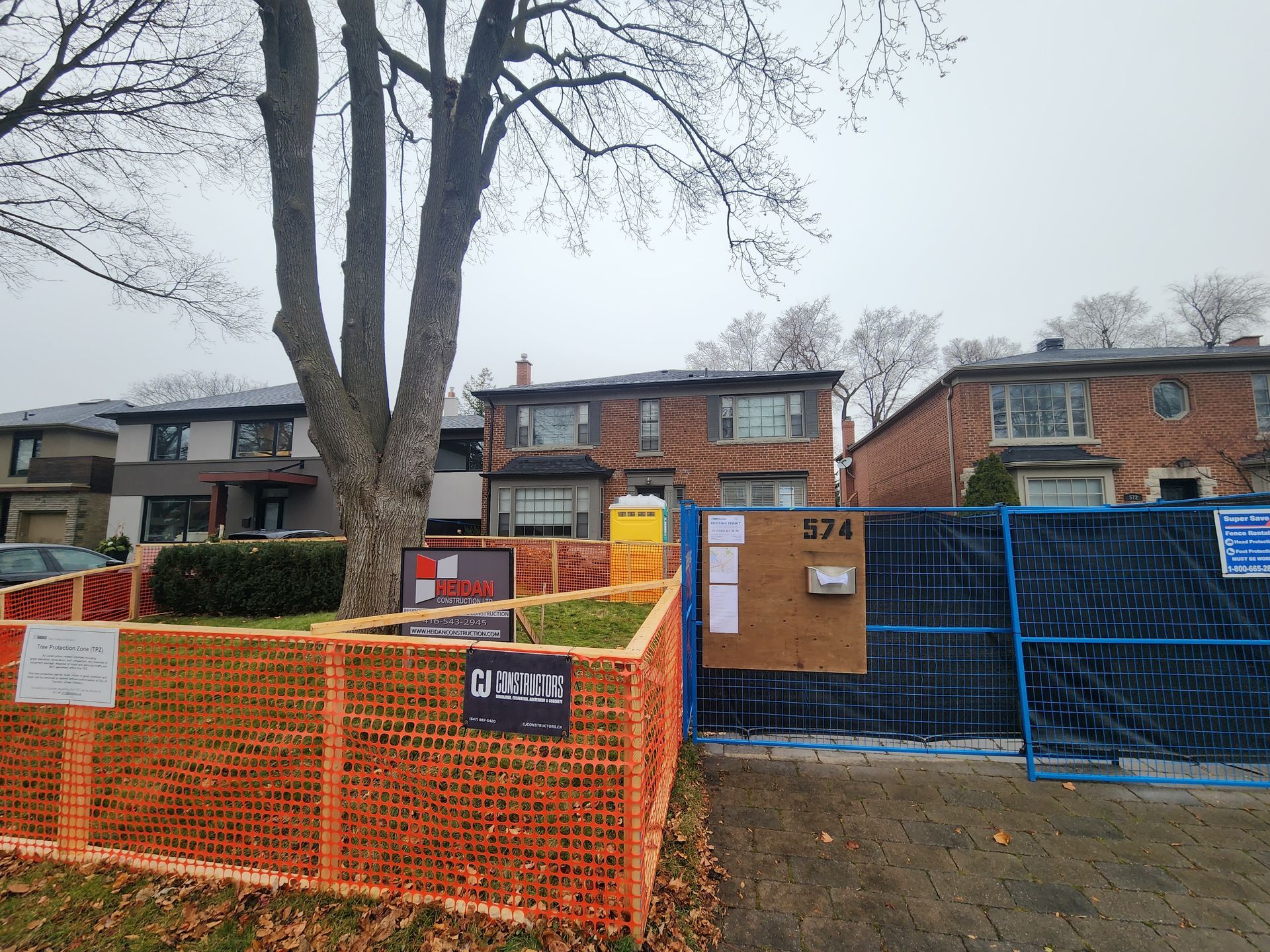 Orange and blue construction fencing around a building entrance under leafless trees
