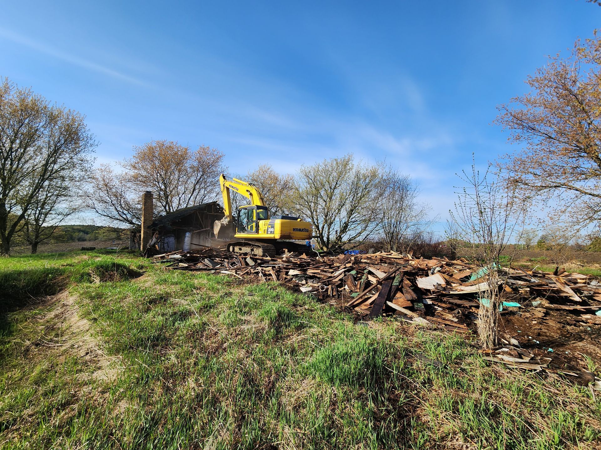 Yellow excavator demolishing a structure beside a pile of rubble under a blue sky